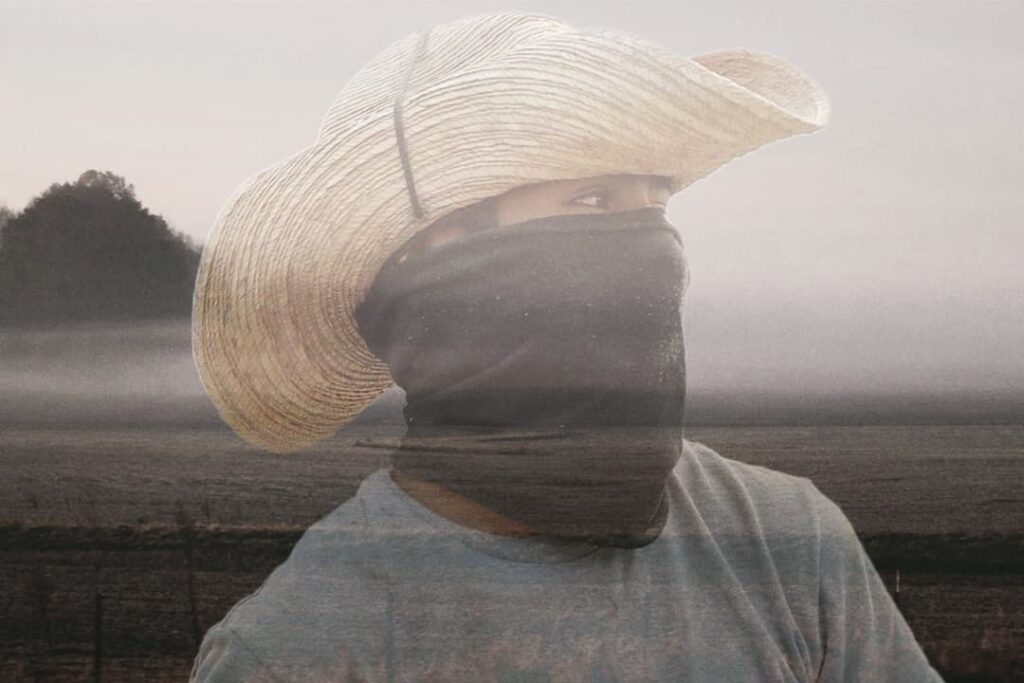 Un hombre que llevaba un gran sombrero de paja y una cara cubierta de pie en un campo brumoso.